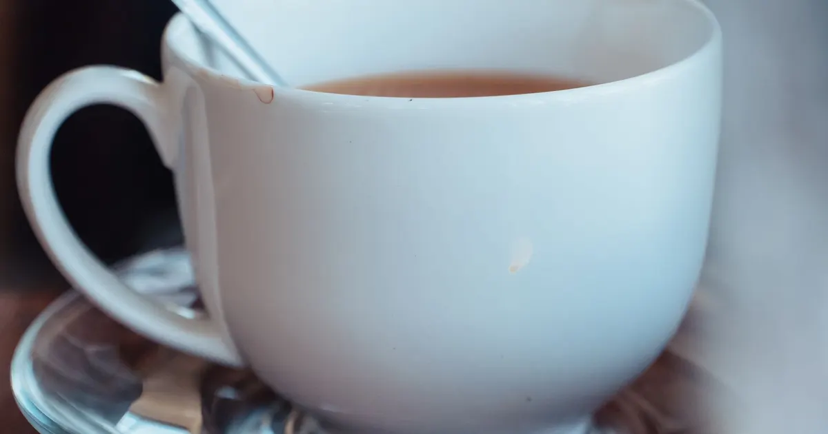A tea bag lifted above a white cup with a drop falling from it, illustrating tea bag brewing speed and the choice between CTC and orthodox leaf