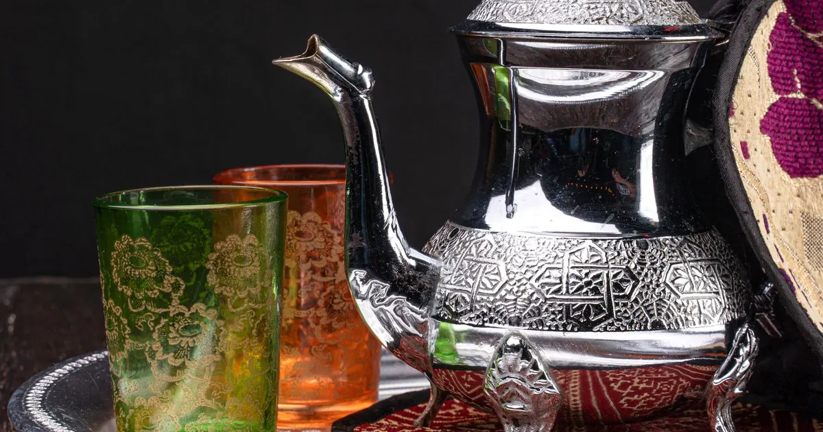 A silver teapot and two patterned glass tea cups on a tray, a typical Middle Eastern tea service for green tea in the Middle East