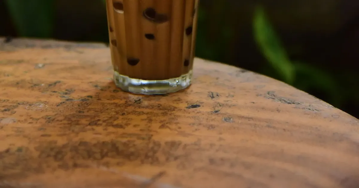 An iced milk tea with tapioca pearls and a straw in a clear plastic cup, a drink made with green tea for bubble tea shops