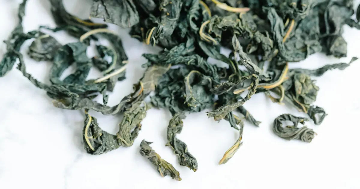 Loose twisted dried green tea leaf spilled on a white surface, showing leaf style relevant to the BOP tea grade and OP grade